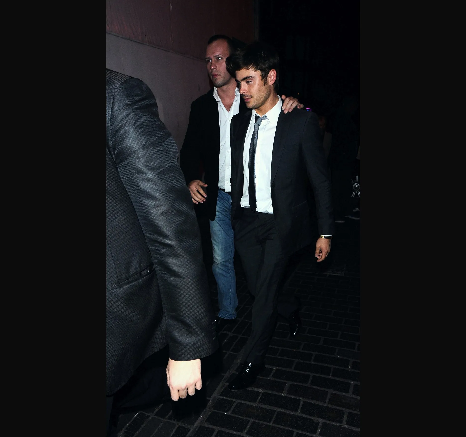 A second frame from the pavement, a moment later, his eyes lowered and one hand at his side.