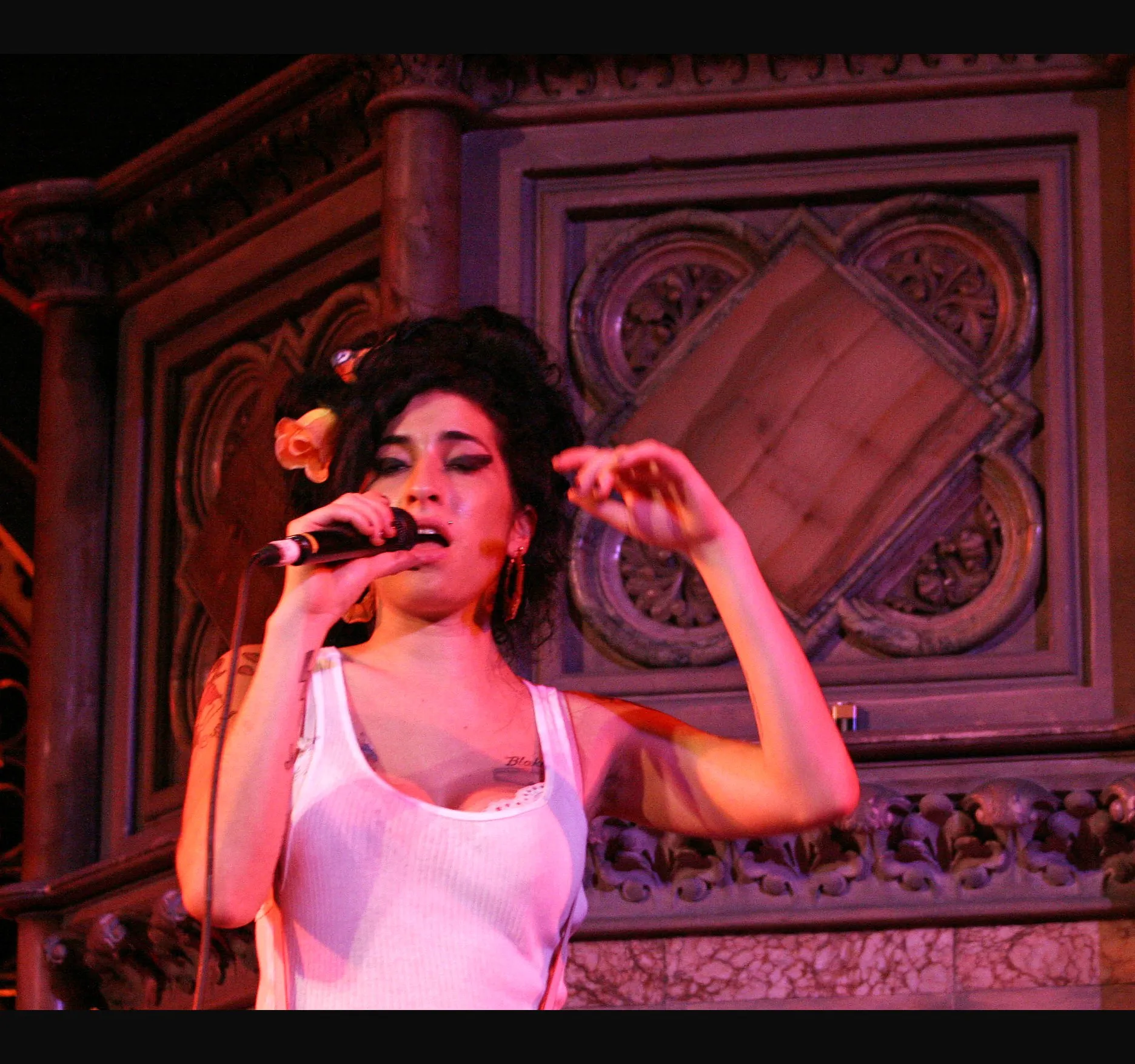 Close up against the chapel's carved panelling, one hand raised as she sings.