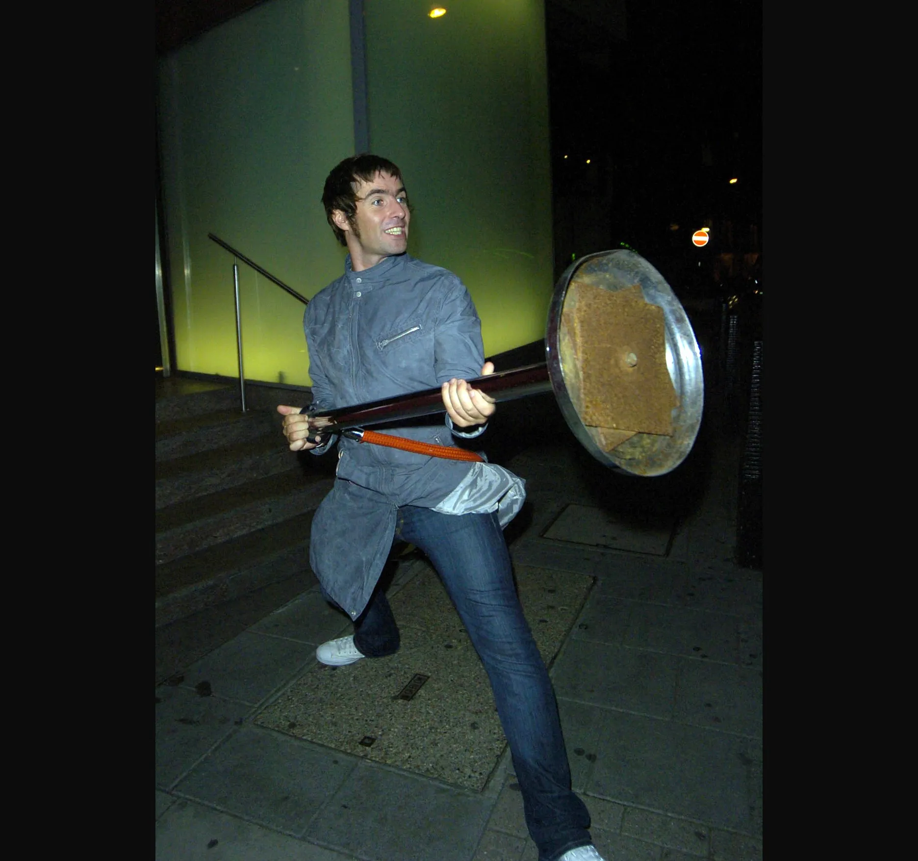 Out on the pavement, smiling, with one of the rope-barrier posts in his hands.