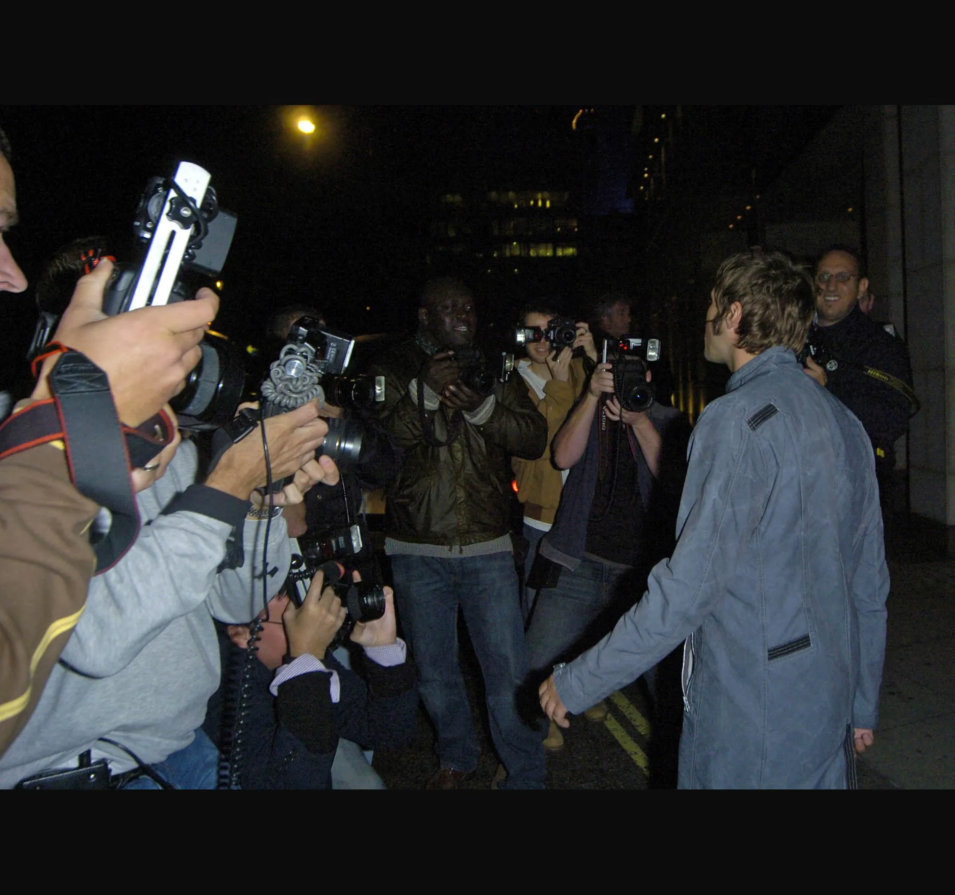 THE STREET. Photographers had gathered outside the bar. Here he is with his back half turned, cameras and flashguns raised all round.