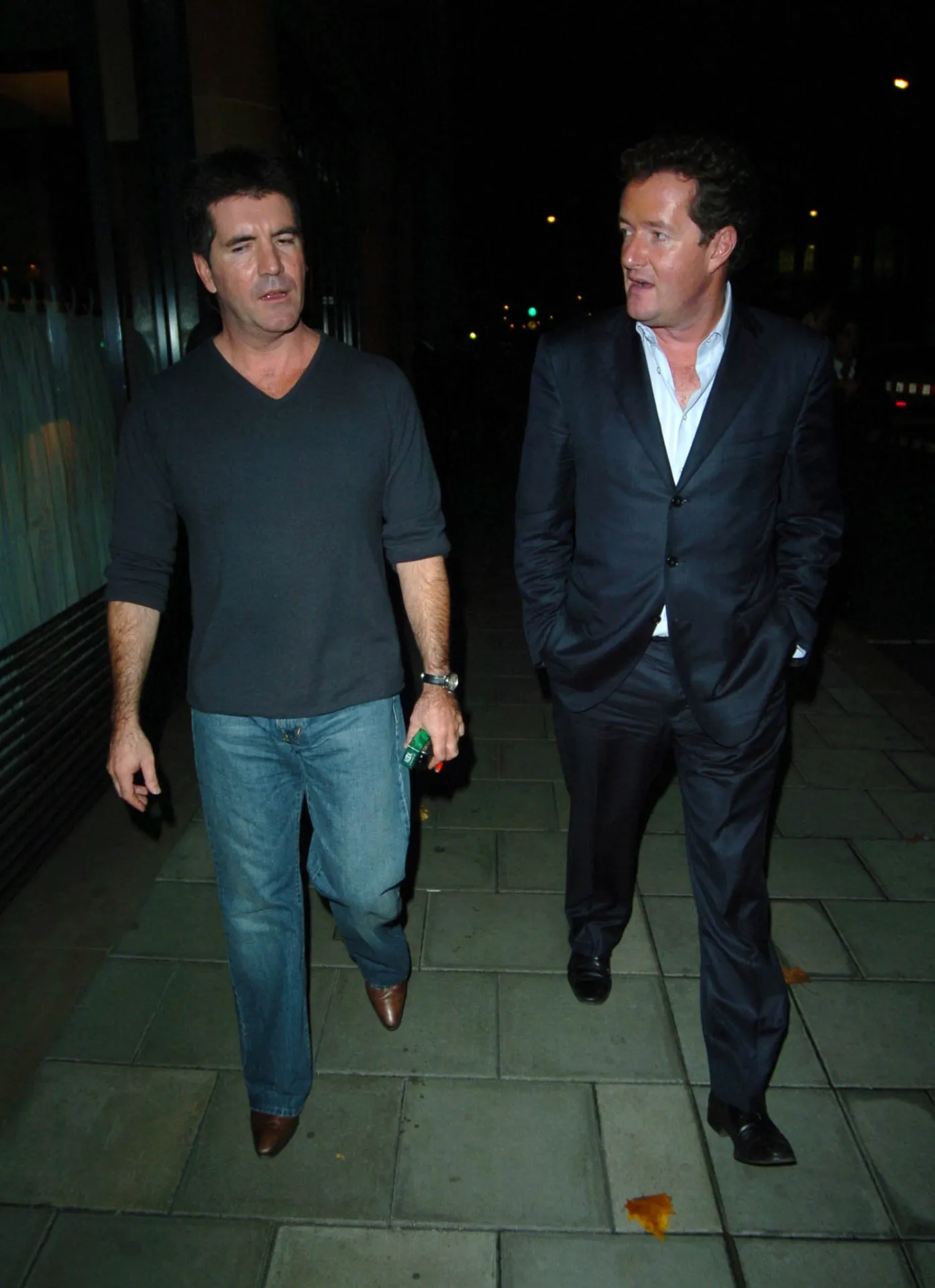 Simon Cowell looks towards the camera while Piers Morgan, in a navy suit and white open-necked shirt, looks across at him as