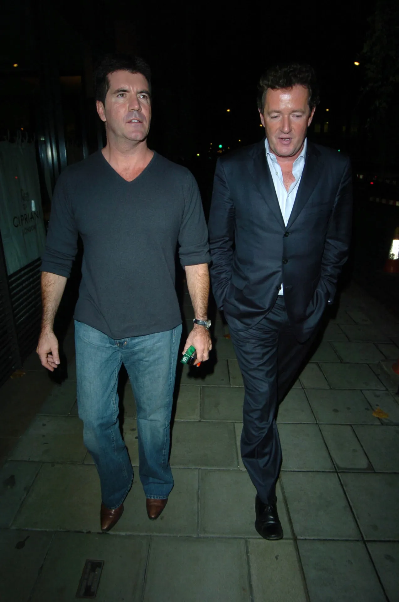 Simon Cowell and Piers Morgan walk towards the camera at night outside Cipriani in Mayfair, both looking straight ahead.
