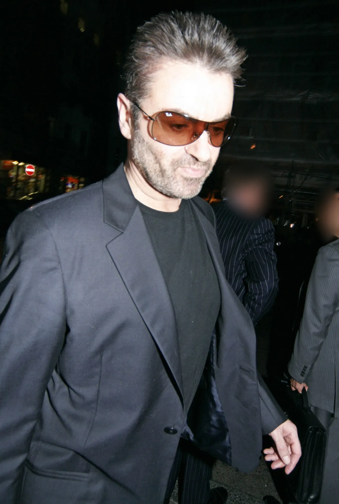 Close view of George Michael in tinted glasses and a charcoal jacket, looking down as he walks into Nobu Berkeley St.