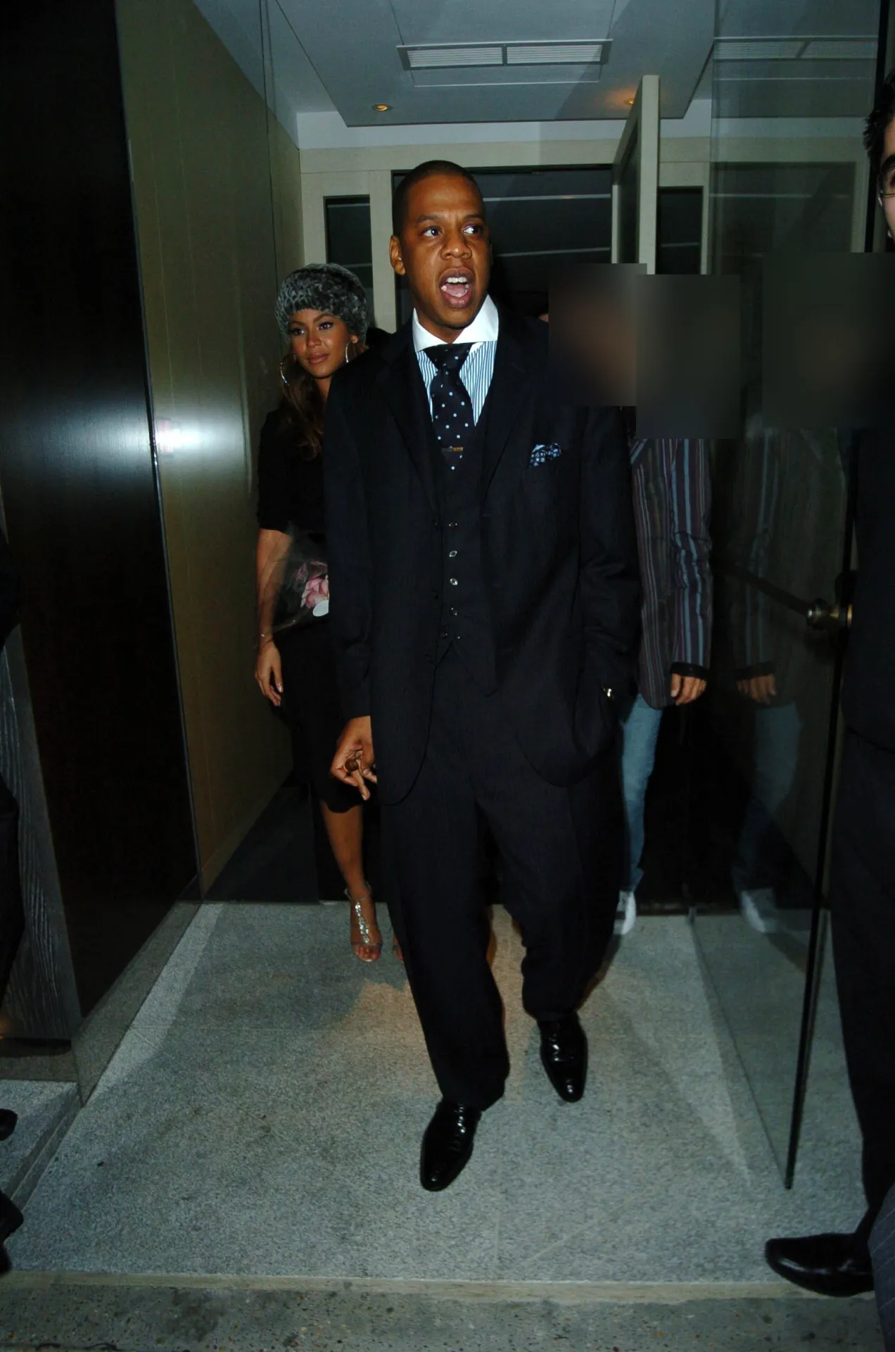 Jay-Z in a dark pinstripe suit and polka dot tie leaving Nobu Berkeley, with Beyoncé behind him.