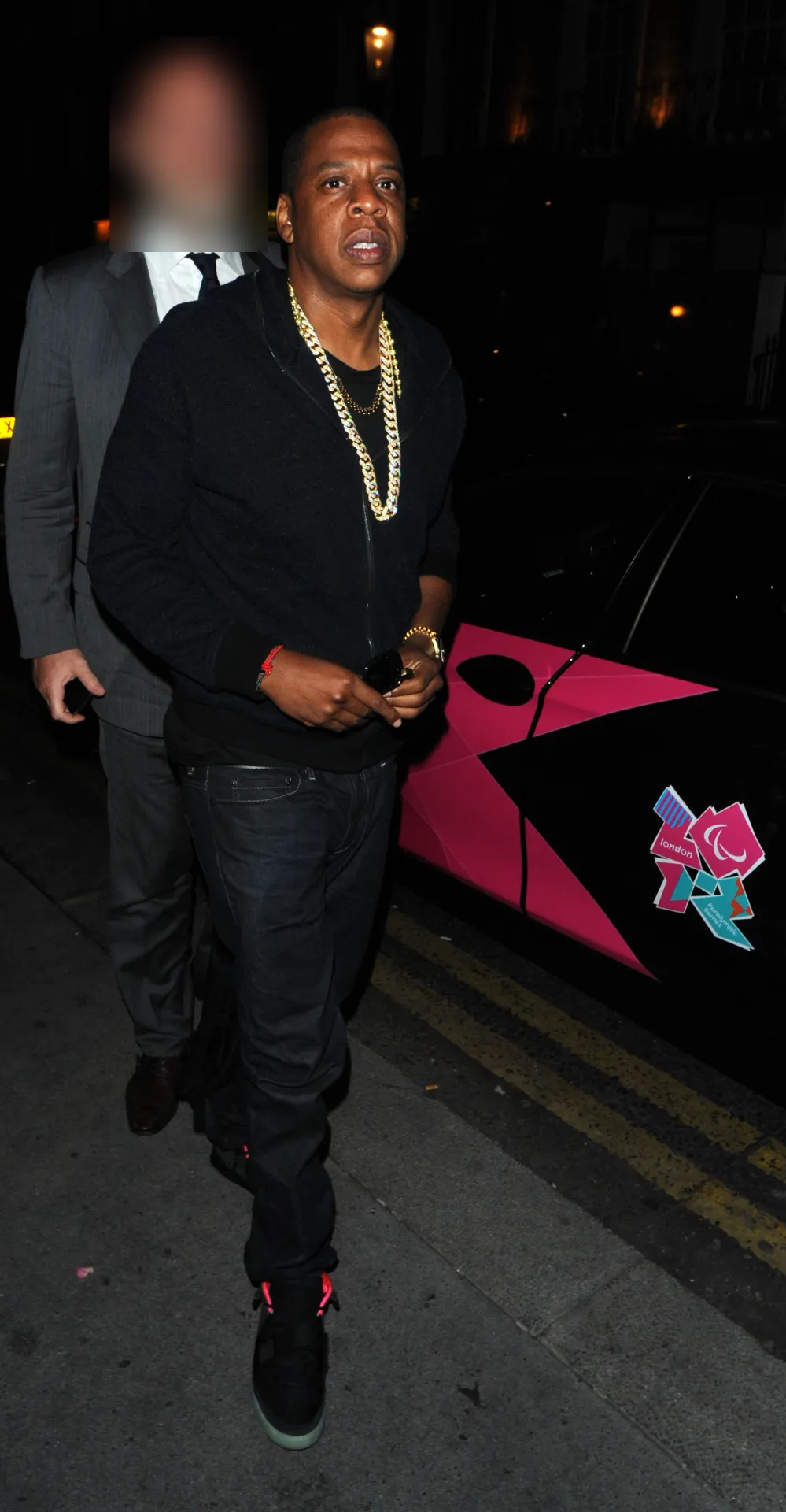 Jay-Z in black with a gold chain arriving at Nozomi in Chelsea beside a London 2012 branded car.