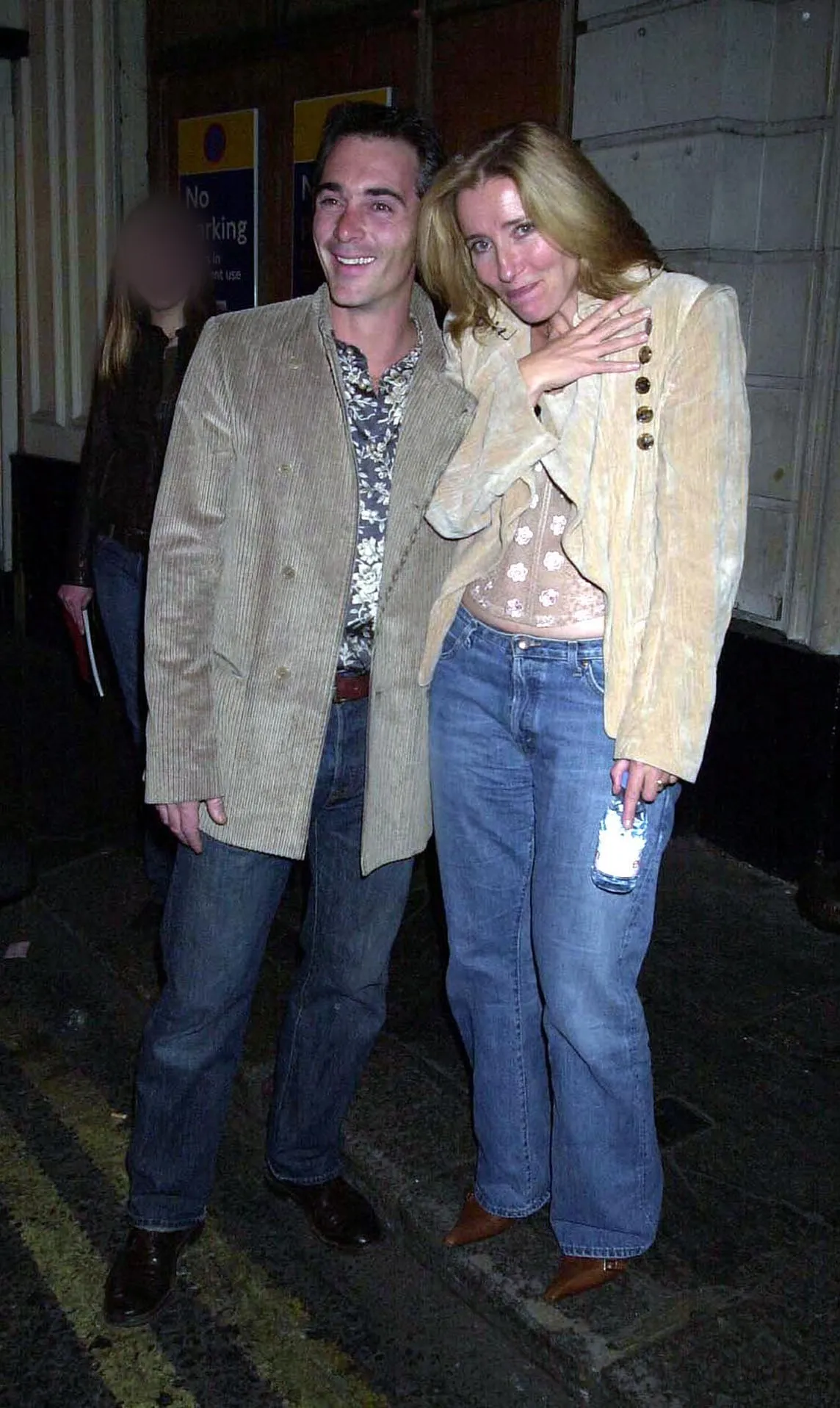 Emma Thompson in a cream jacket and jeans laughing beside Greg Wise on a London pavement at night.